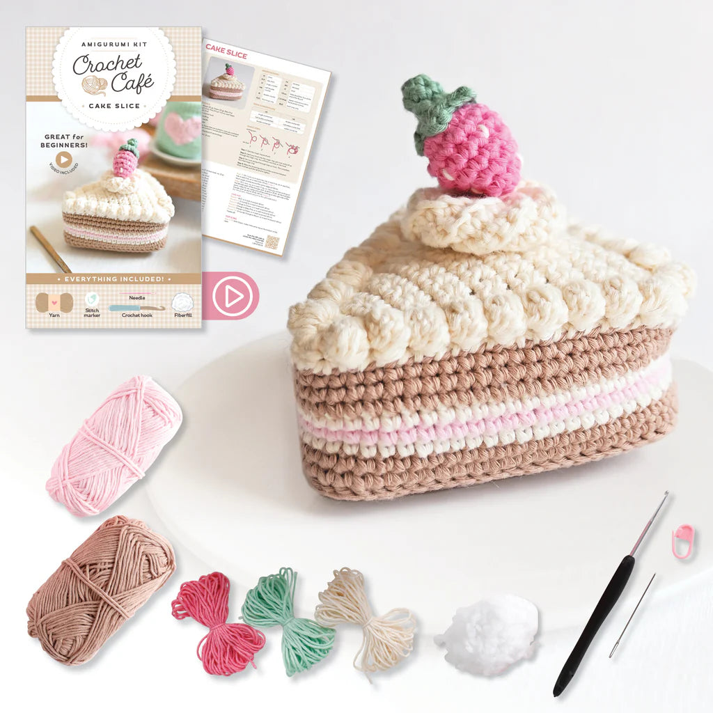 Crocheted cake slice with yarn, hooks, and a pattern leaflet on a white background