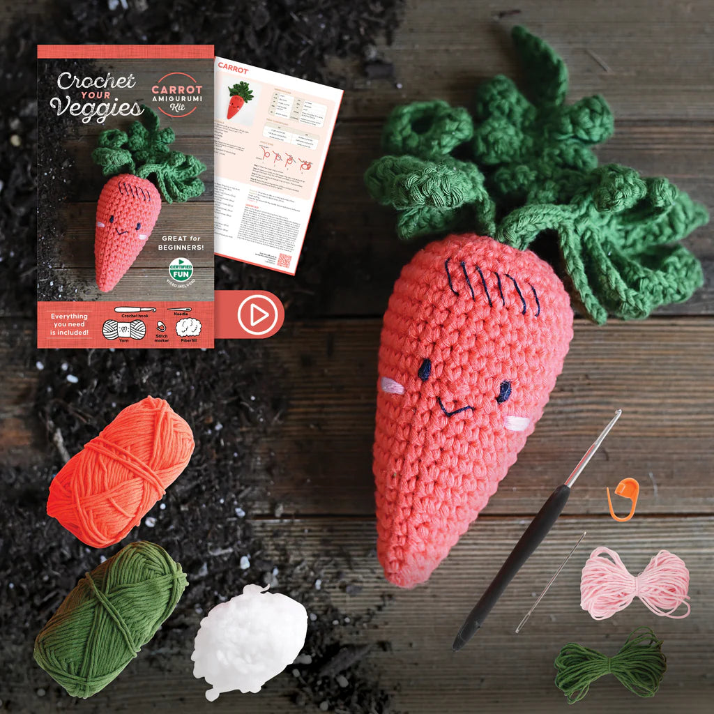 Crocheted carrot toy with yarn, needle, and packaging on a wooden surface