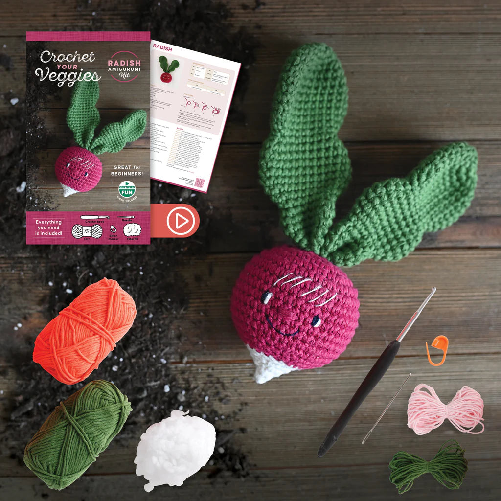 Crocheted smiling radish with yarn, crochet hook, and pattern on a wooden surface