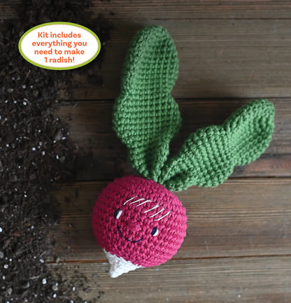 Crocheted radish with green leaves on a wooden surface, surrounded by soil.