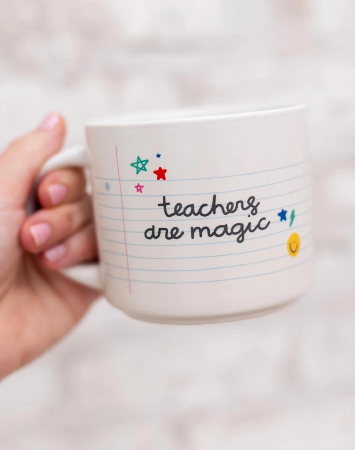 Mug with 'teachers are magic' text held by a hand against a blurred background