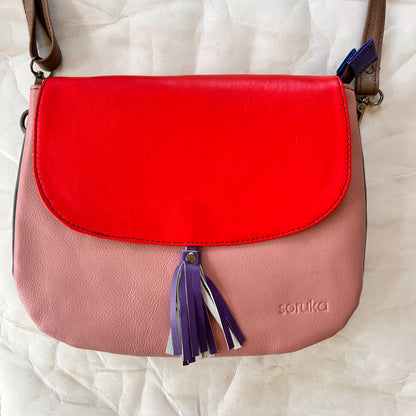 lola bag with bright red flap with purple tassel over a pink body.