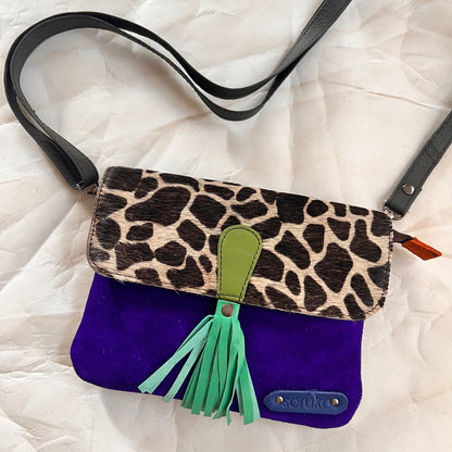 juliette bag with animal print flap, green tassel, and crossbody strap clipped on it.