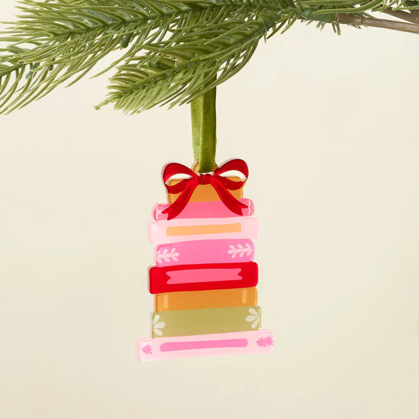 Colorful stacked book ornament with a red bow hanging from a Christmas tree.