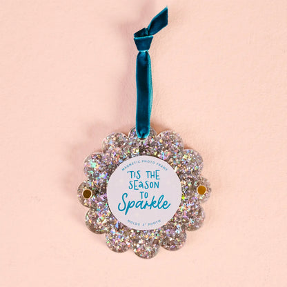 silver glitter Scalloped Acrylic Frame Ornament with a blue hanging ribbon shown on a beige background