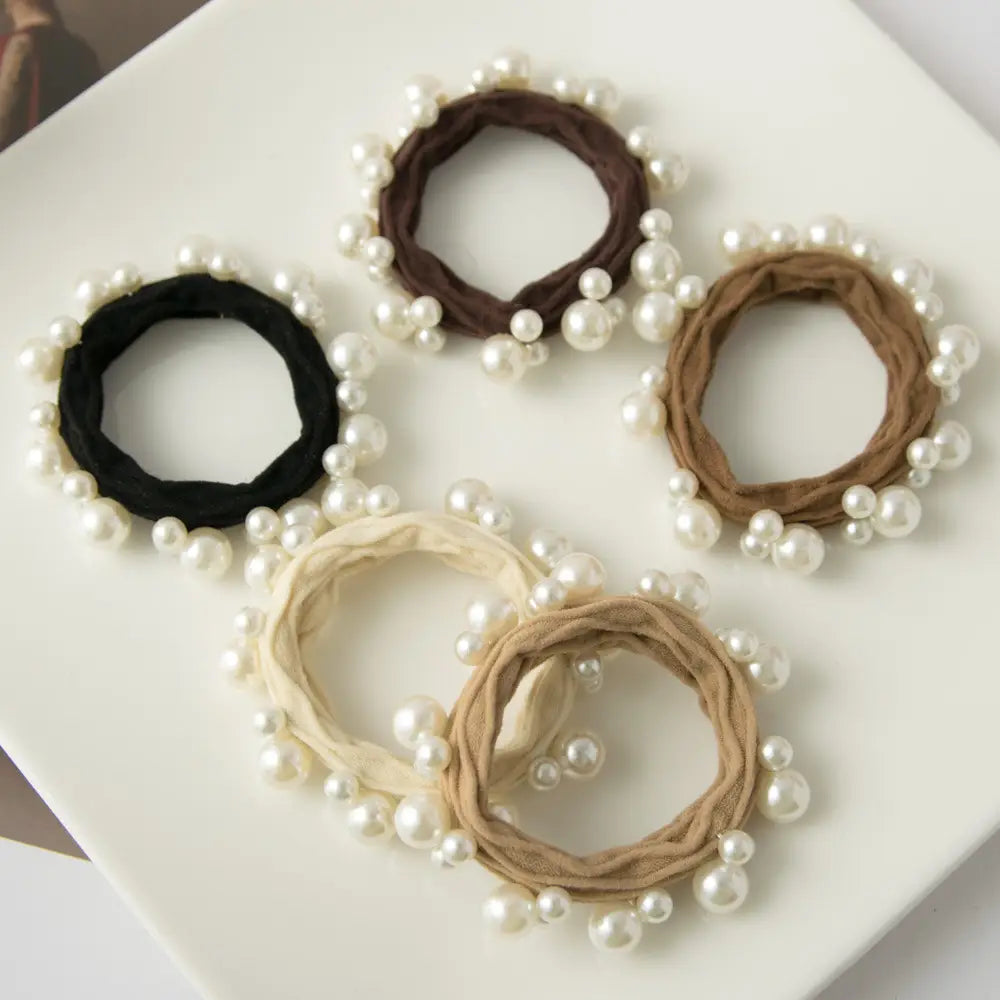 5 hair ties in black and brown hues with pearls on them arranged on a white tray