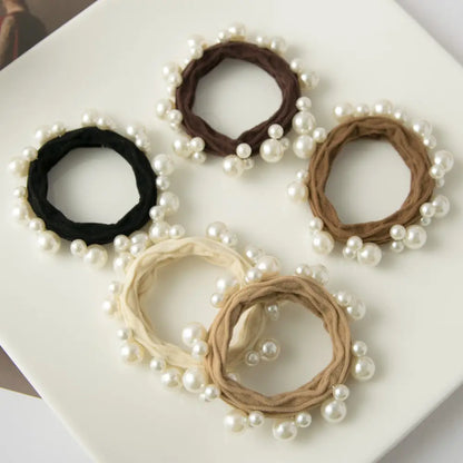 5 hair ties in black and brown hues with pearls on them arranged on a white tray