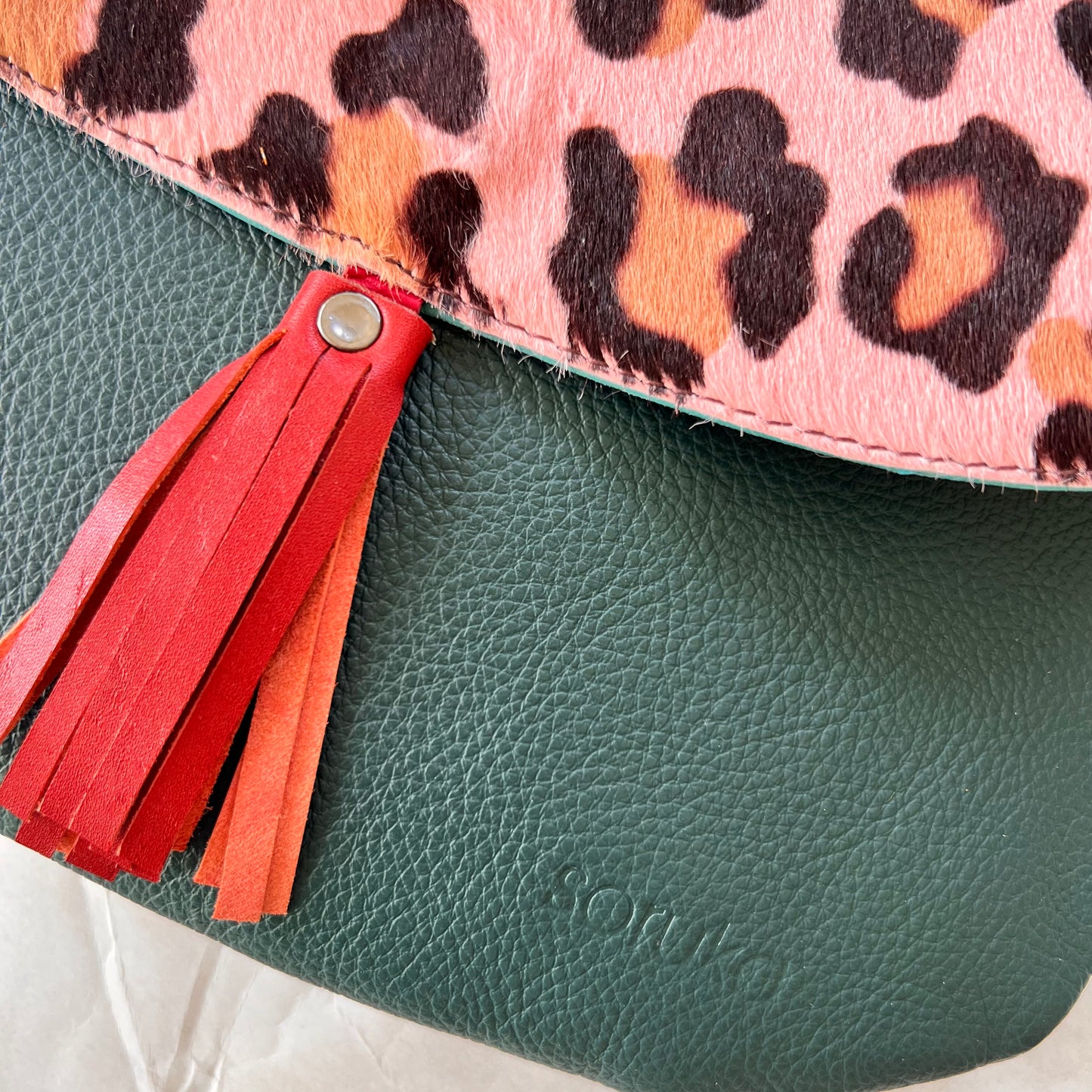 close-up of lola bag with pink cheetah print hair-on-hide flap with rusty colored tassel over a deep green body.