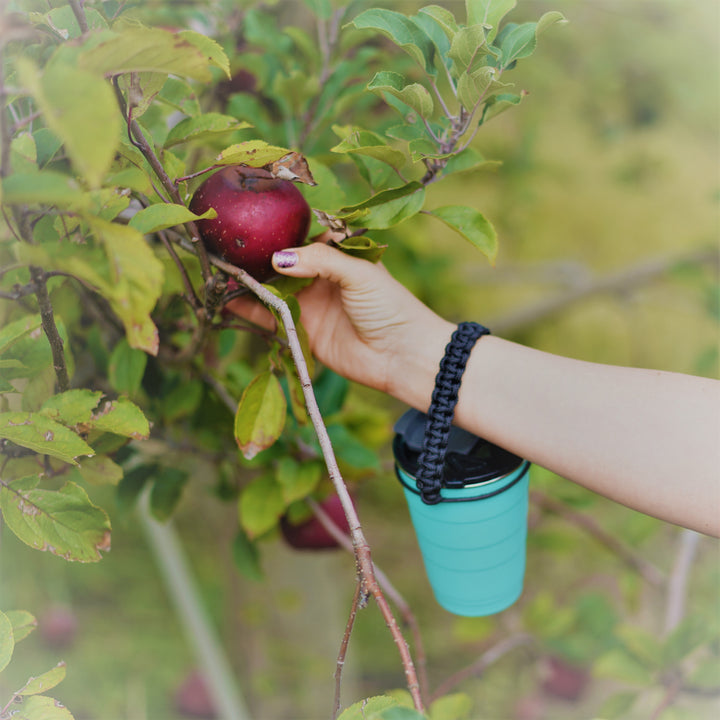 black adventure handle on a pirani life tumbler hanging on a person's wrist while they pick apples.