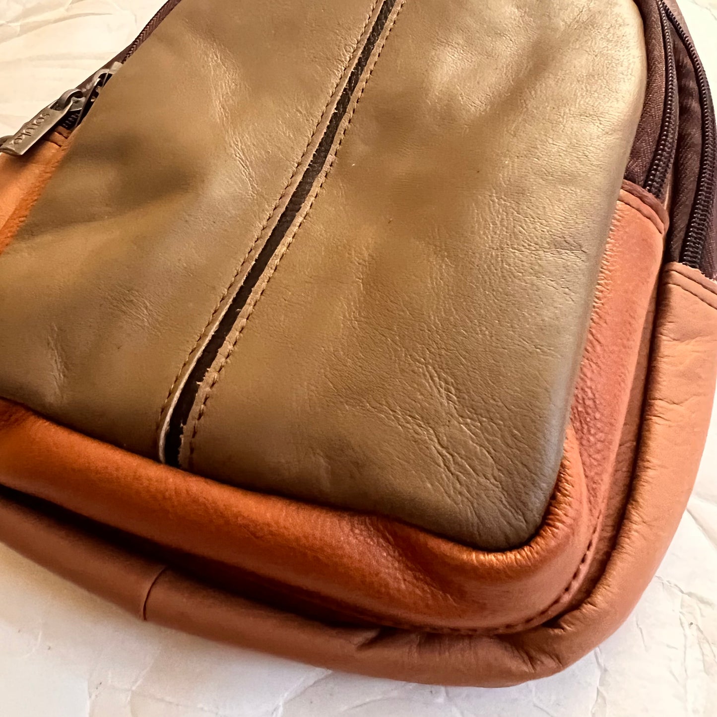 close-up of bottom corner of taupe Gregg sling bag.
