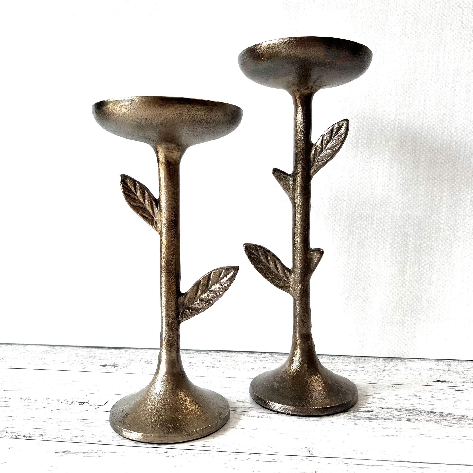 2 sizes of metal candle holders with leaves on the stems on a white background.