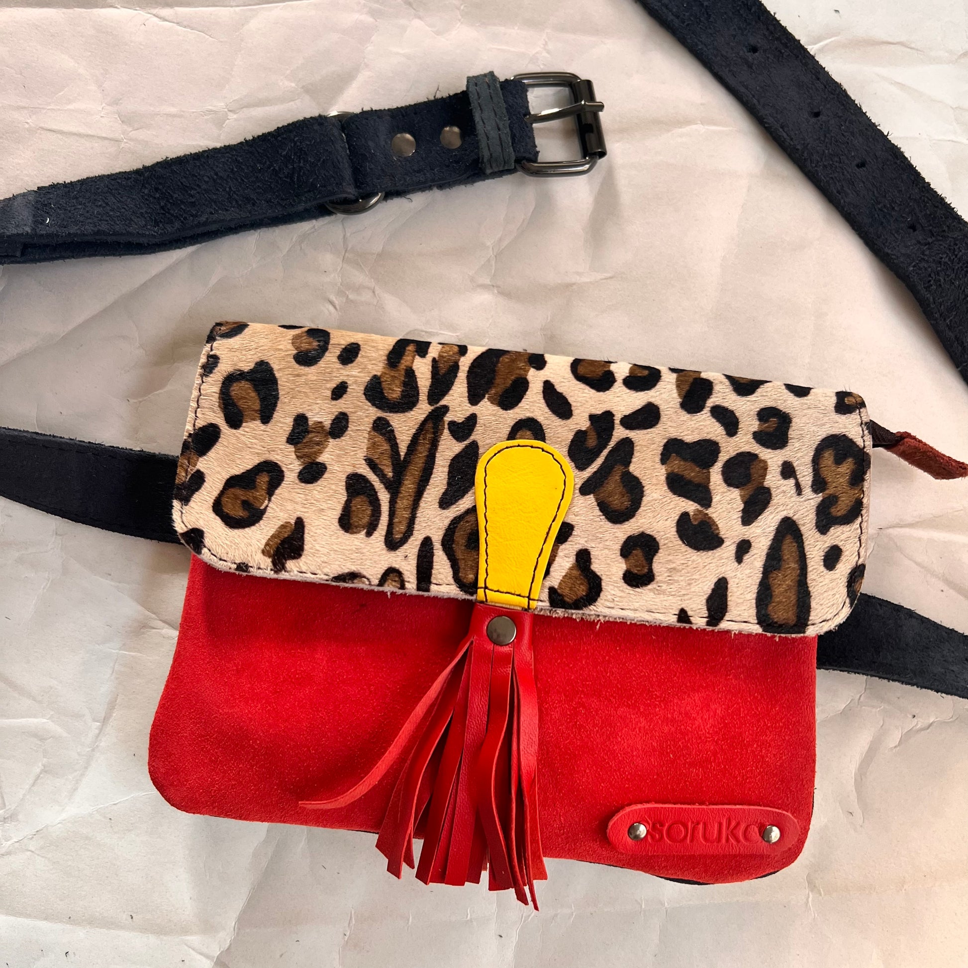 juliette bag with animal print flap, red tassel, and belt arranged with it.