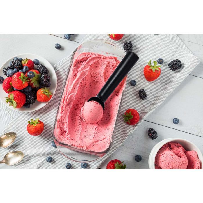 Antifreeze ice cream scoop in a dish of strawberry ice cream set on a table and surrounded by other berries