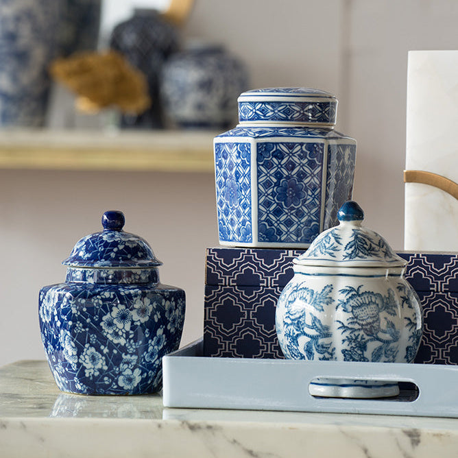 Blue and white porcelain ginger jars arranged on a light gray tray on a marble surface, with a matching patterned box behind them in a softly styled interior setting.