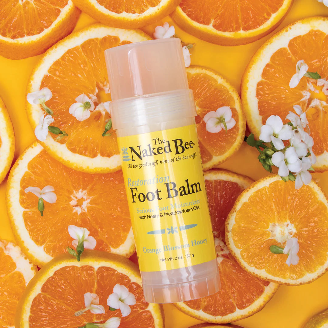 Naked Bee Foot Balm on a background of orange slices and flowers
