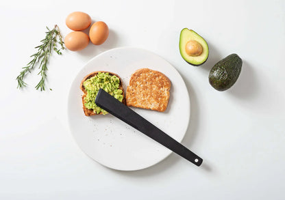 Avocado toast on a white plate with avocados, eggs, and a black utensil on a light background