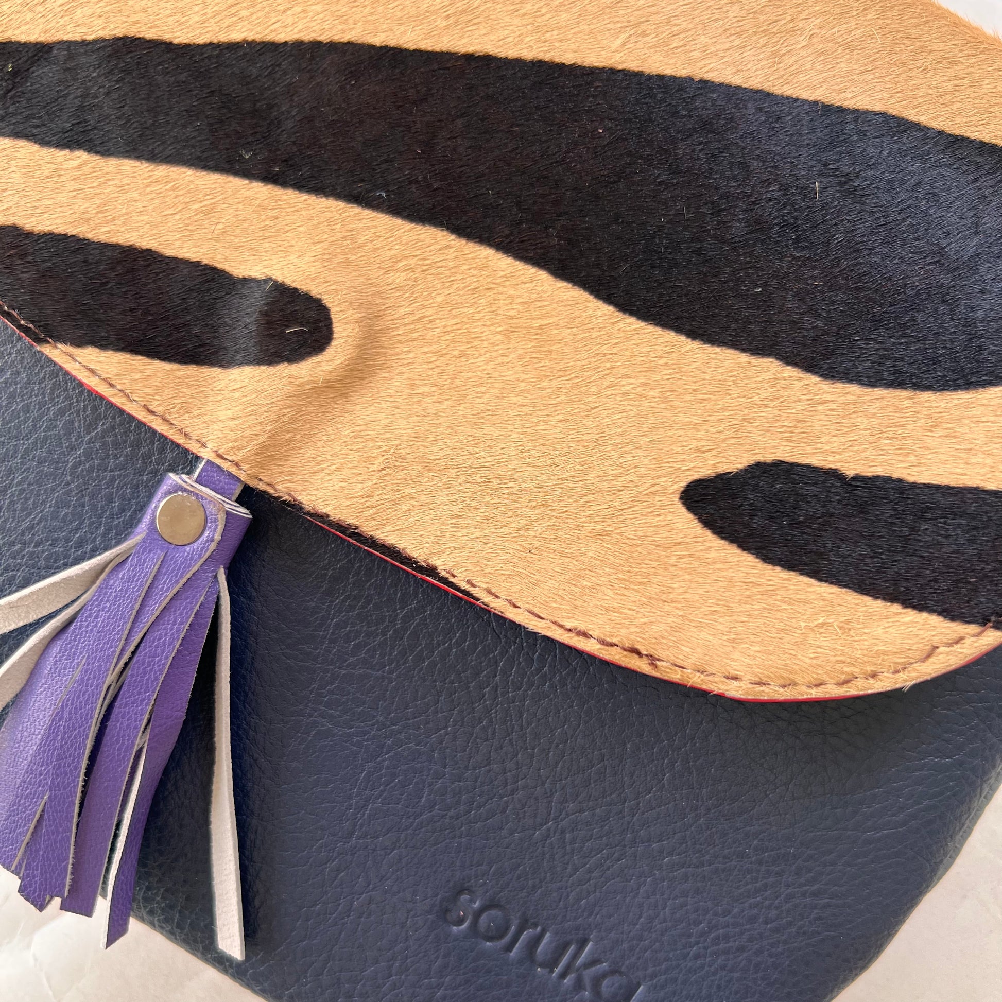 close-up of lola bag with animal print hair-on-hide flap with purple tassel over a navy body.