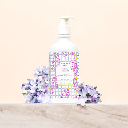 bottle of lilac dream hand and body lotion printed with liliac flowers and a grey palid background with lilac flowers arranged around it.