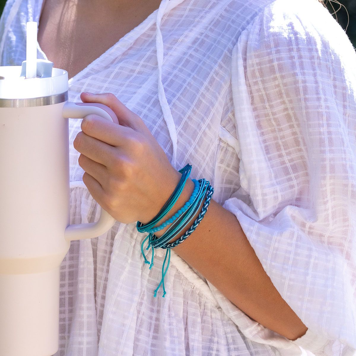 person wearing a white top, holding a beverage tumbler and wearing ocean depths Weave & Wander Bracelets