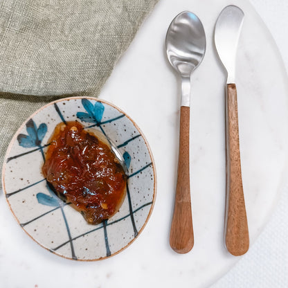 small spoon and spreader on a table with a bowl of jam and a napkin.