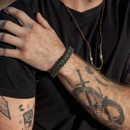 person with tattoos on arm wearing a black shirt and green and black woven bracelet