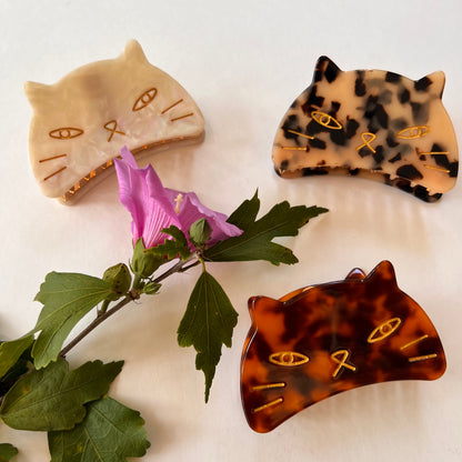 3 styles of cat face hair clips arranged with a flower.