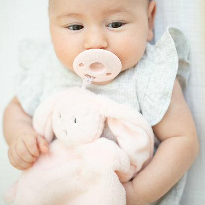 another baby holding bunny lovey with pacifier in their mouth.