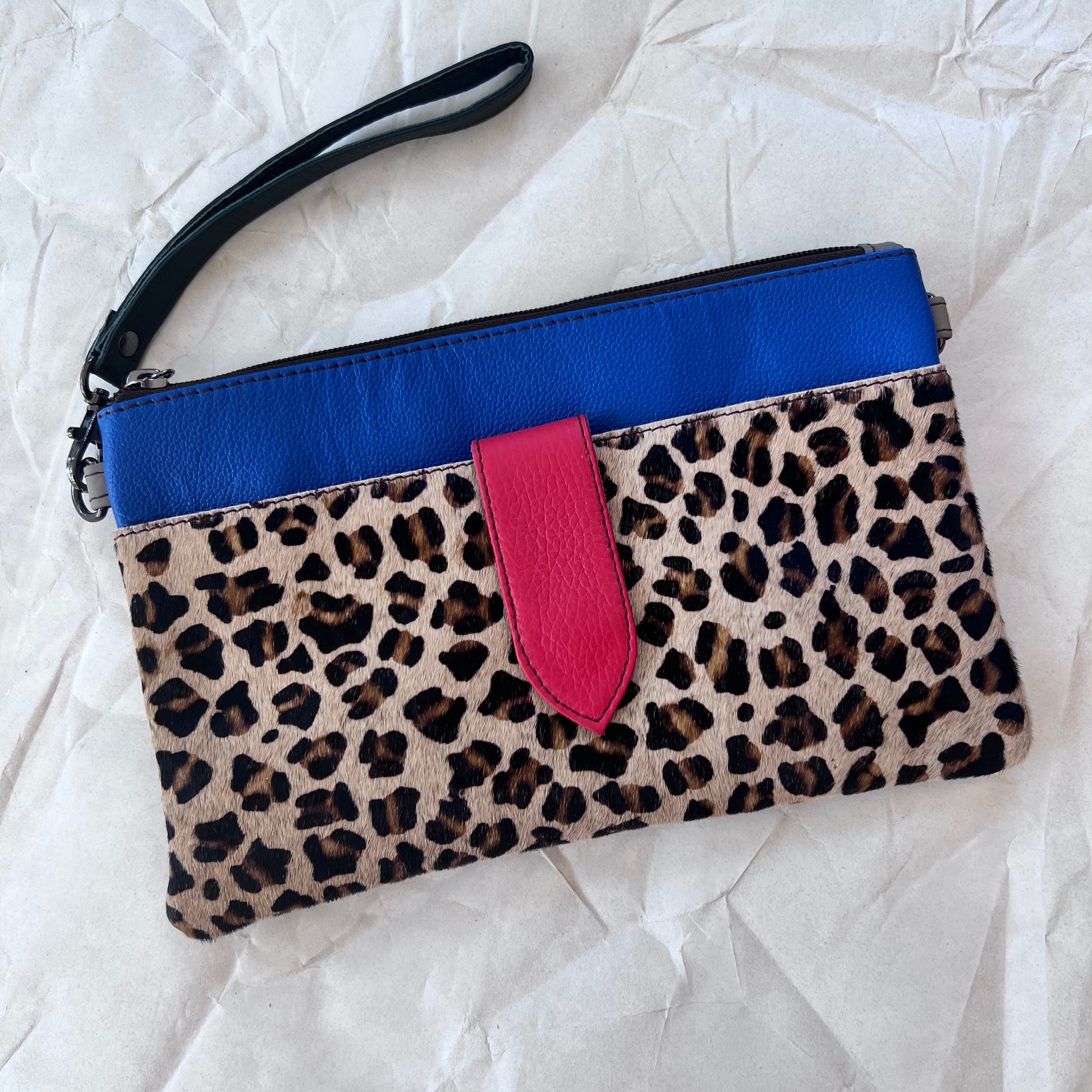 blue rectangular bag with cheetah print pocket, purple tab, and wristlet strap.
