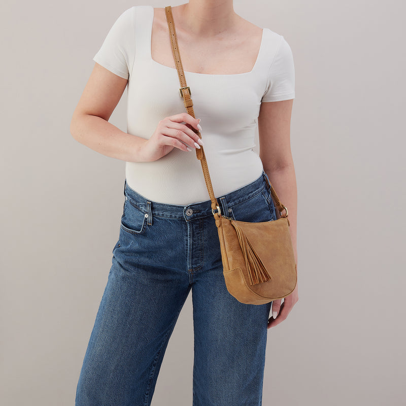 Person wearing a white top and blue jeans with a brown leather bag on a plain background