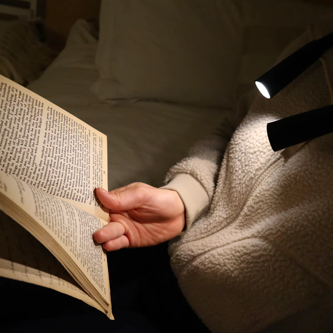 person sitting in bed reading using the flexible neck lamp.