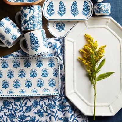 White bamboo platter with a yellow flower laying on it, arranged on a table with other blue and white dishes.