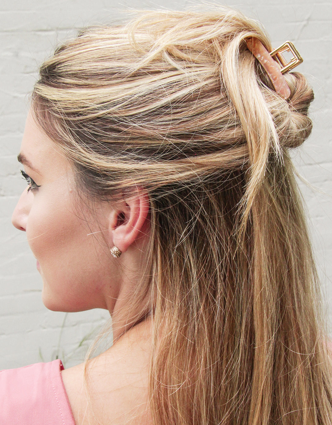 blonde person with a blush claw clip holding half of their hair in a messy bun.
