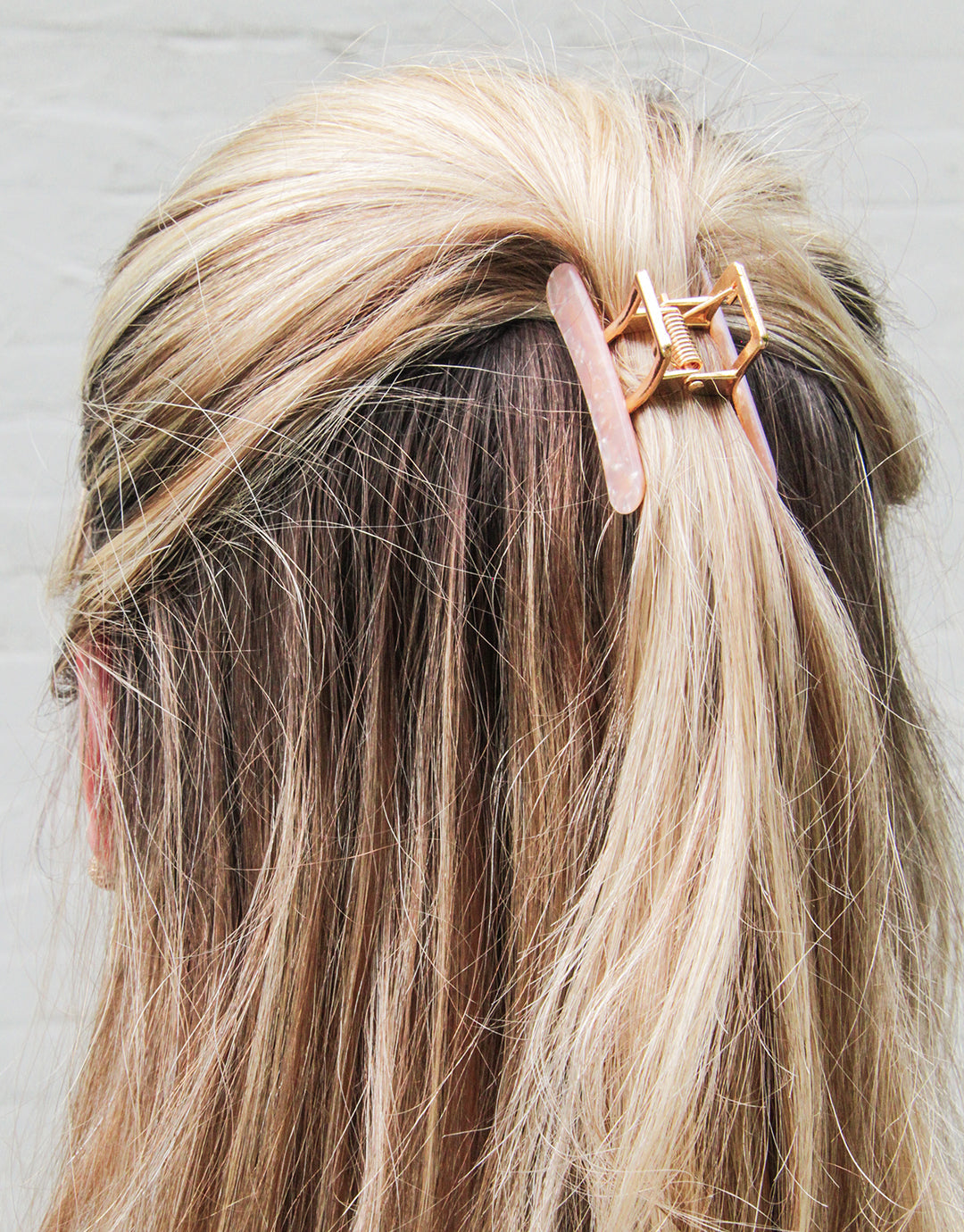 back view of blonde person white top potion of their hair held up with a neutral colored claw clip.