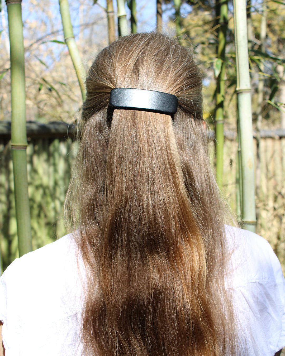 person with light brown hair with half of it clipped with a black wooden barrette.