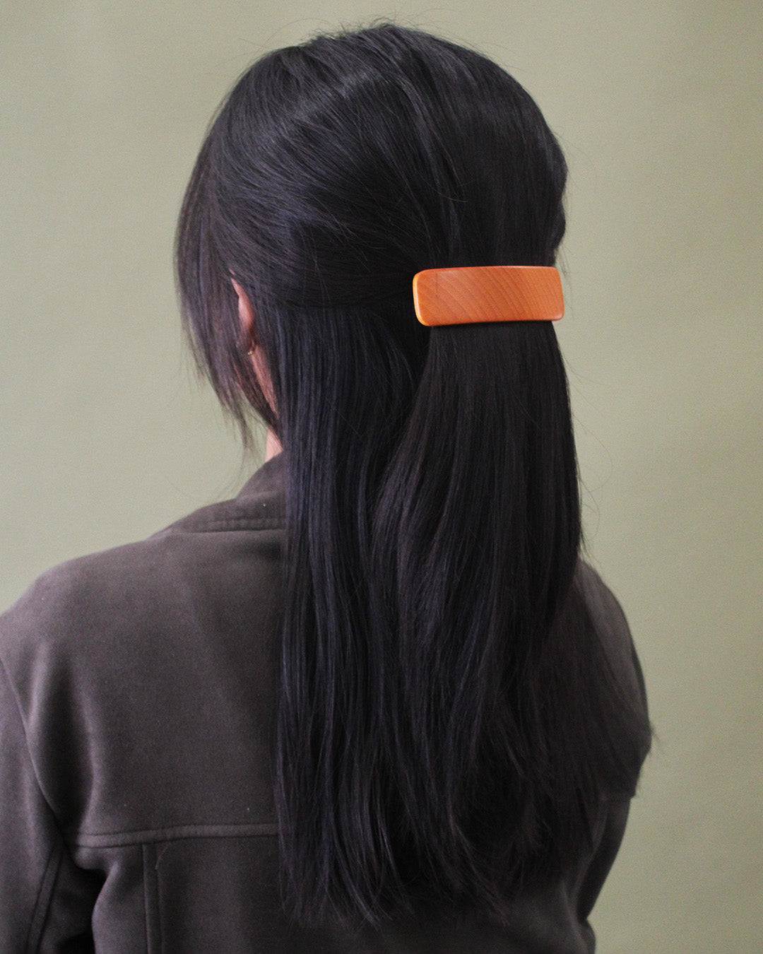 person with long black hair wearing it half up clipped with a brown wooden clip.