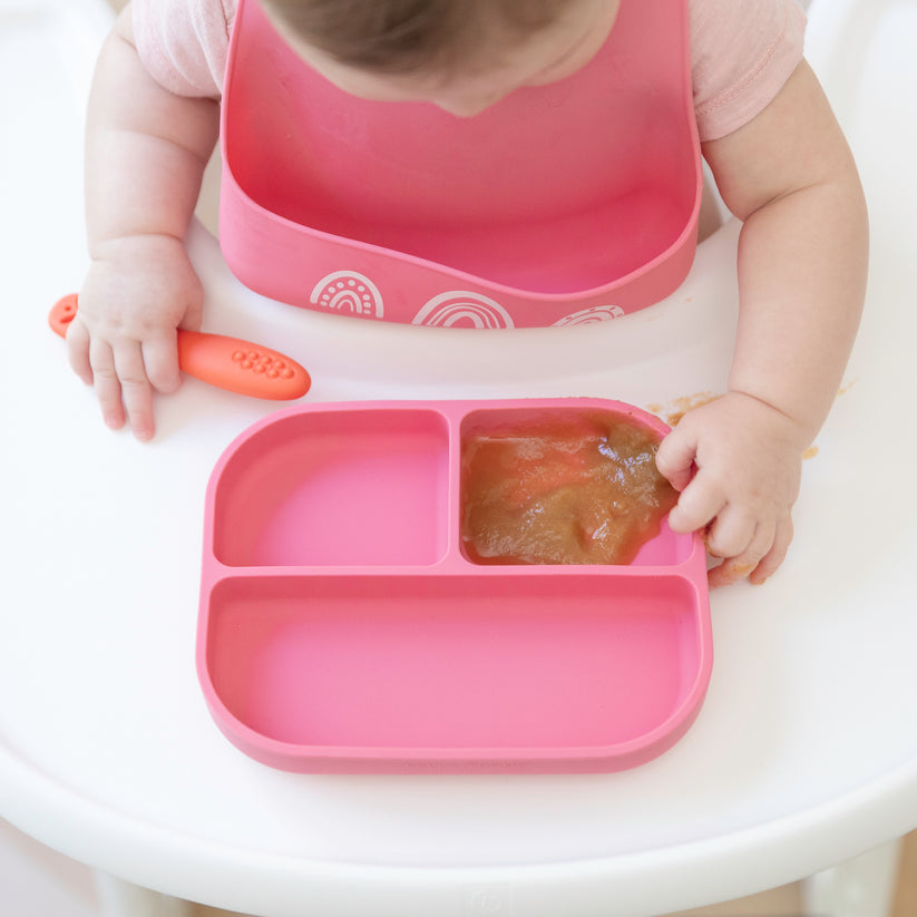 top view of baby sitting in highchair with pink plate of pureed foods.