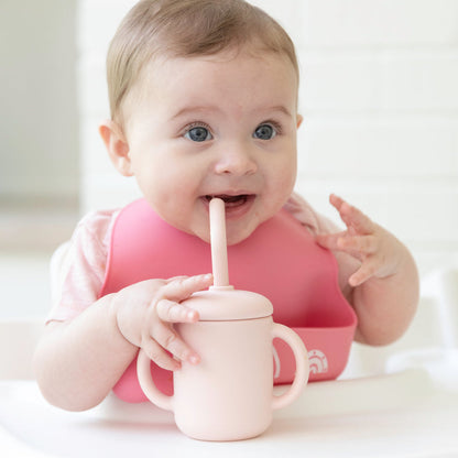 baby sitting in highchair with pale pink cup with straw lid.