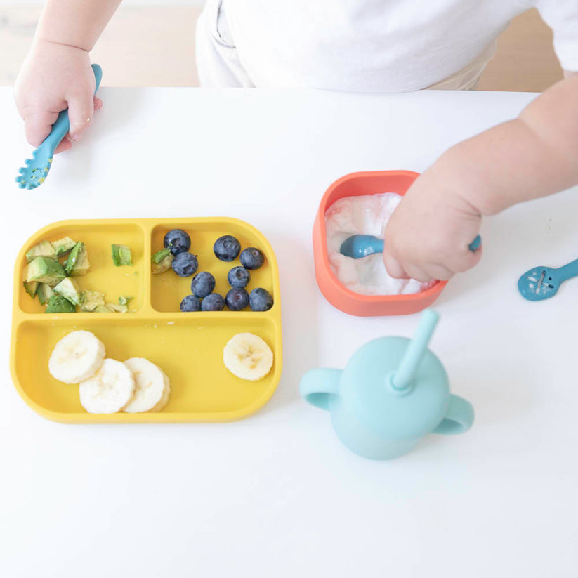 top view of baby feeding themself from silicone dishes.