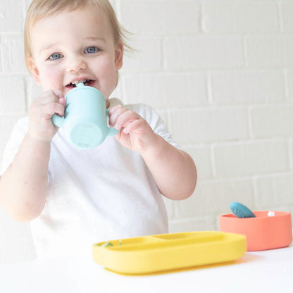 toddler drinking from light blue silicone cup with straw.