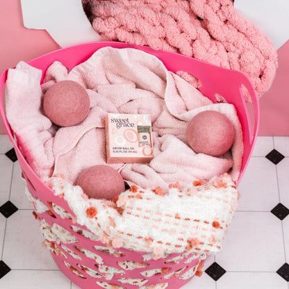 Pink laundry basket with pink towels, pink balls, and a box of oil on a checkered floor.