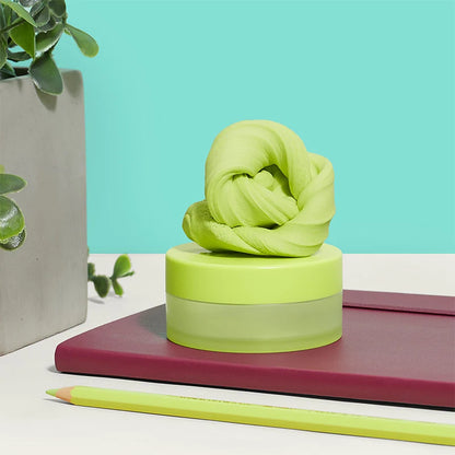Green putty in a knot-shaped set on a cylindrical base with a plant and notebook in the background