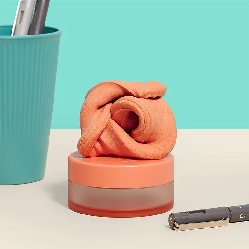orange fidget puttey set on its Coral-colored container  on a light beige surface with a teal background