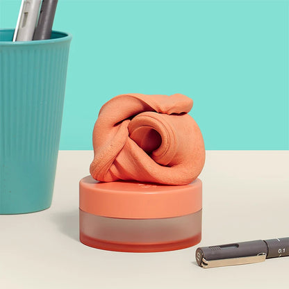 orange fidget puttey set on its Coral-colored container  on a light beige surface with a teal background