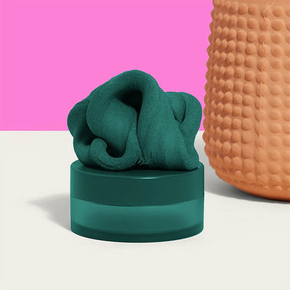 dark green fidget putty set on its container with a terracotta vase next to it on a pink background