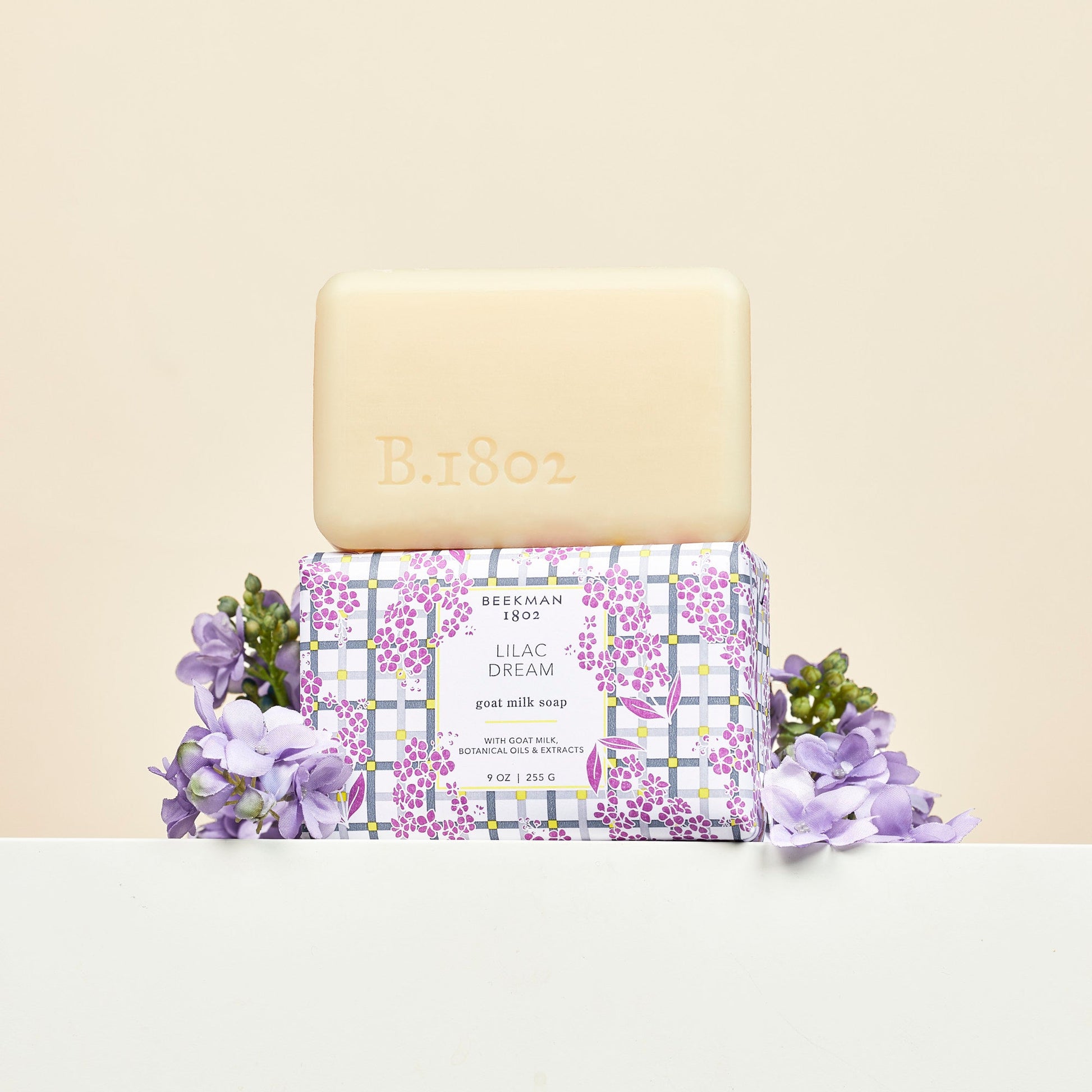 bar of lilac dream soap stacked on another bar wrapped in paper packaging with lilac flowers arranged around it.