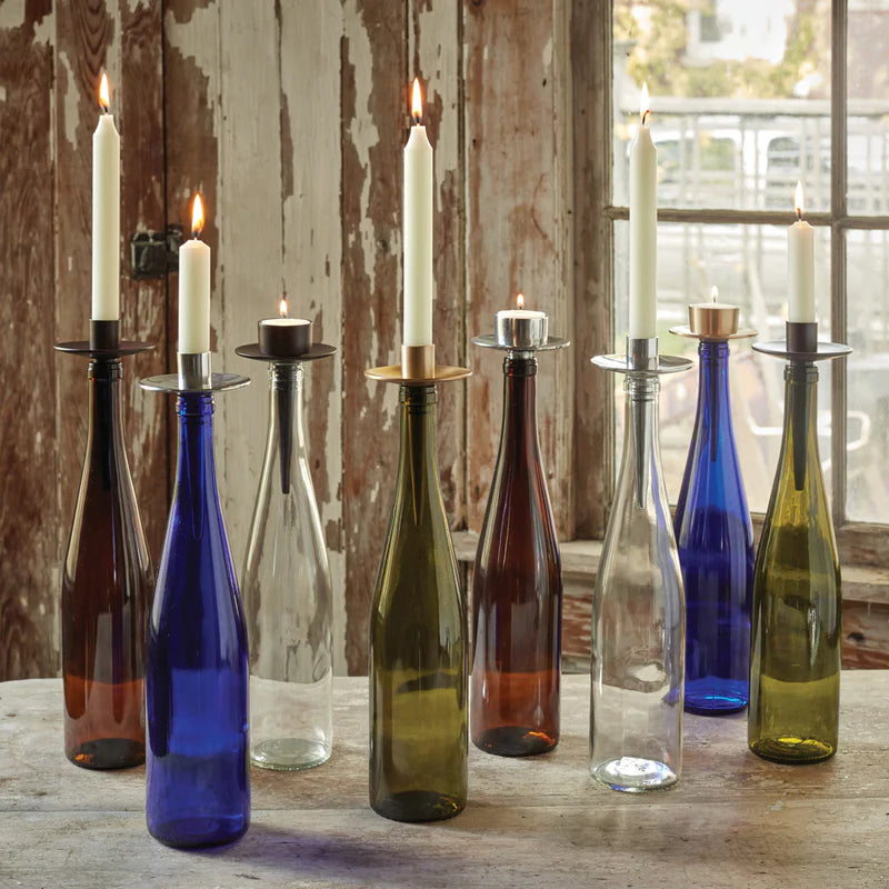 serveral colorful empty wine bottles with bottlabras in them arranged on a wooden table in front of a window.