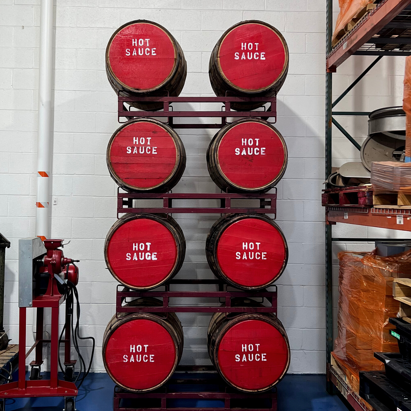 bourbon barrels stacked in a rack with red lids painted in white with "hit sauce".