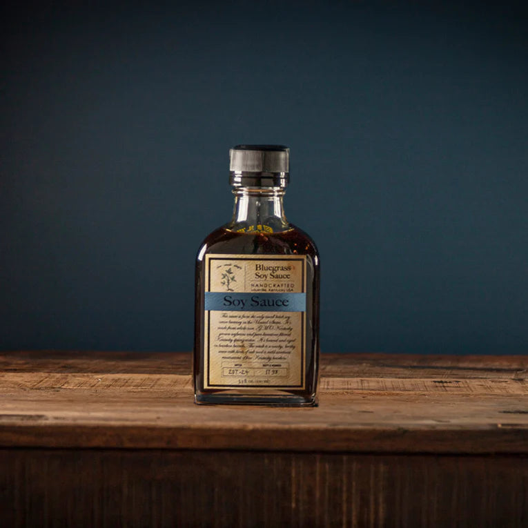bottle of Bluegrass Soy Sauce set on a wooden table against a blue background