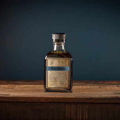bottle of Bluegrass Soy Sauce set on a wooden table against a blue background
