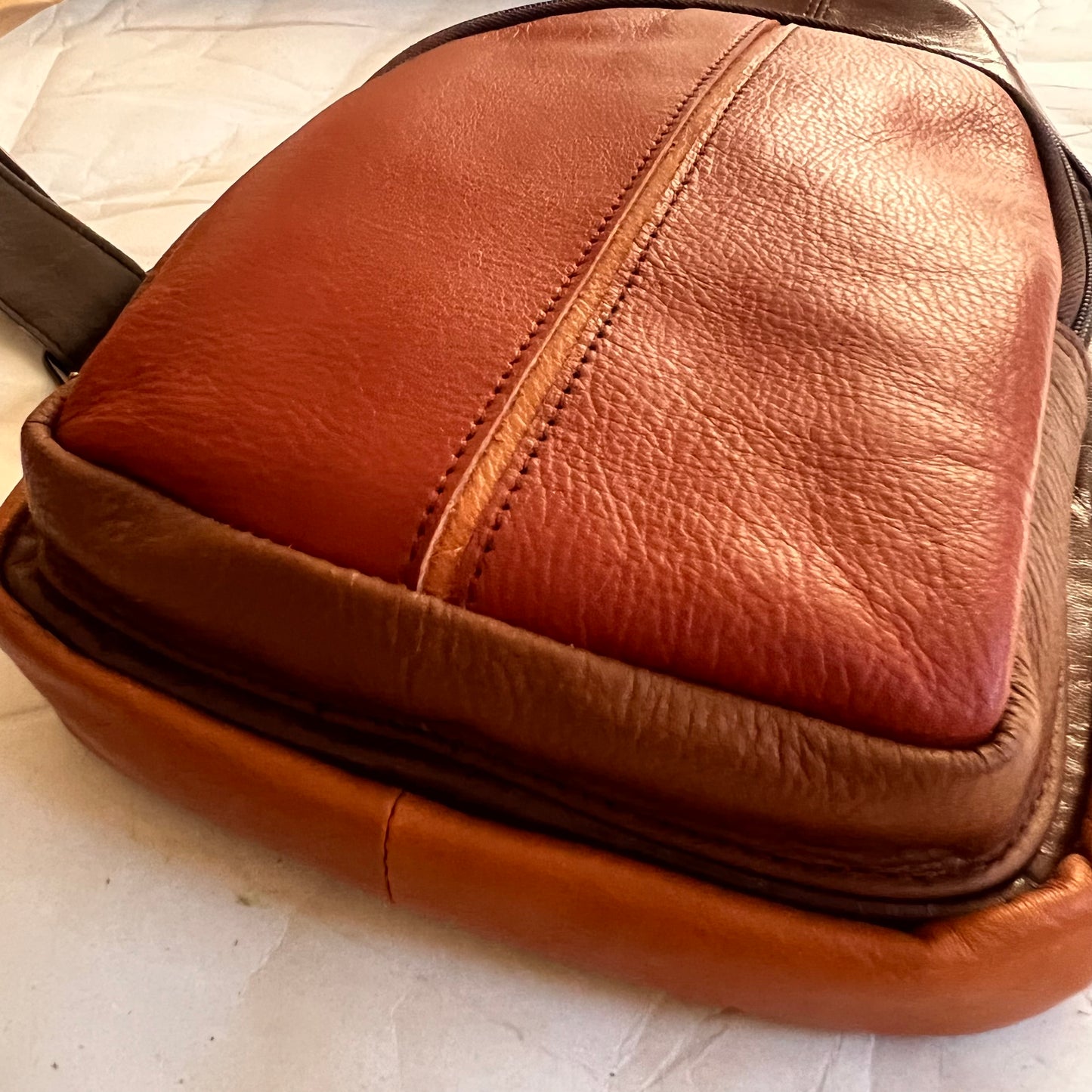 close-up of bottom corner of rust Gregg sling bag.
